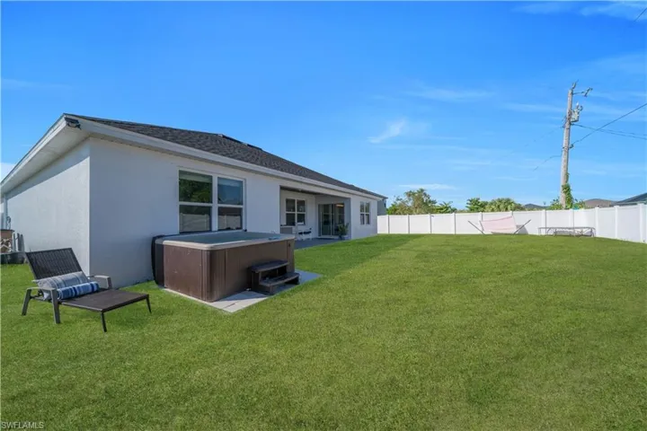 Rear view of house featuring a hot tub, a patio, stucco siding, a fenced backyard, and roof with shingles