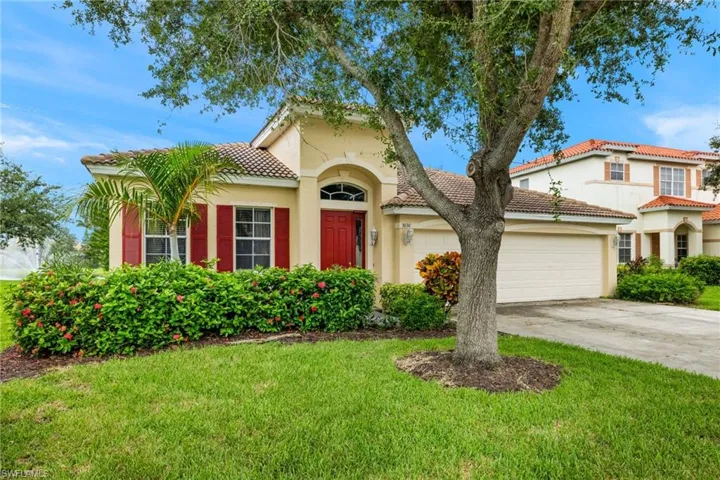 Exterior featuring a two-car garage, red entry door, red window shutters, and a well-maintained lawn with mature landscaping