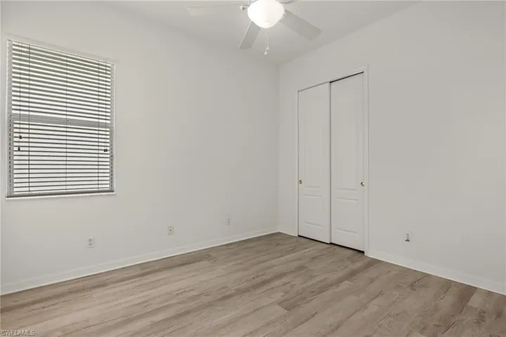 Wood-finish flooring, ceiling fan, window with blinds, and white bi-fold closet doors