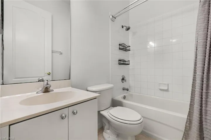 Bathroom featuring a vanity with an integrated sink and cabinet storage, a toilet, and a bathtub with white tile surround
