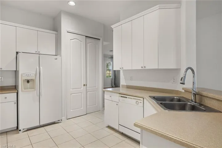 White cabinetry with crown molding, dual basin stainless steel sink, chrome gooseneck faucet, light-toned countertops, and tile flooring