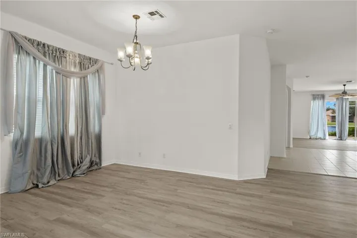 Spacious interior featuring wood-finish flooring, a window with blinds, and a chandelier with frosted glass shades