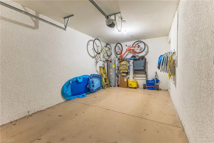 Garage with a textured wall, electric water heater, and a garage door opener
