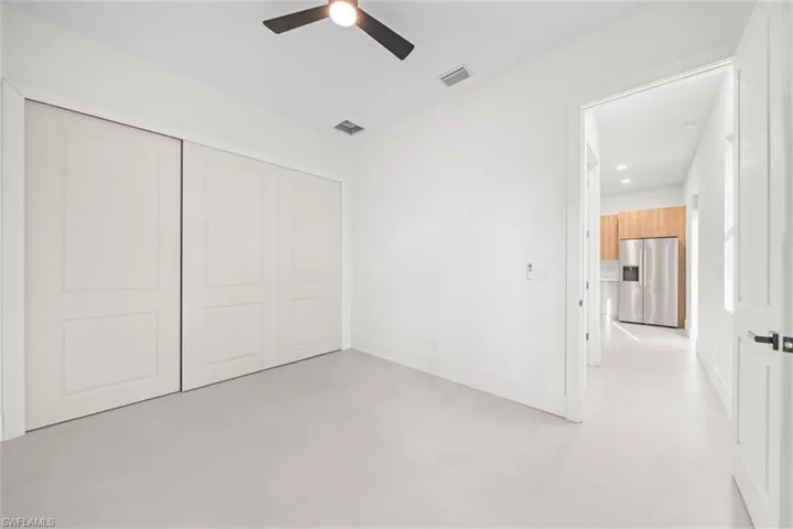 Unfurnished bedroom with stainless steel refrigerator with ice dispenser, finished concrete floors, a closet, a ceiling fan, and recessed lighting
