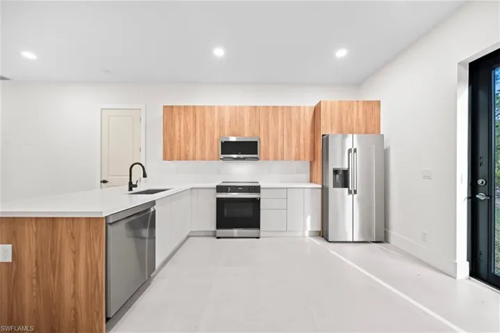 Two tone kitchen with modern cabinets, stainless steel appliances, a peninsula, recessed lighting, and light stone counters
