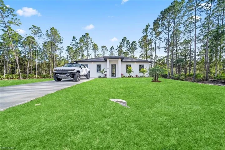 Prairie-style home with stucco siding, a front lawn, driveway, and view of scattered trees
