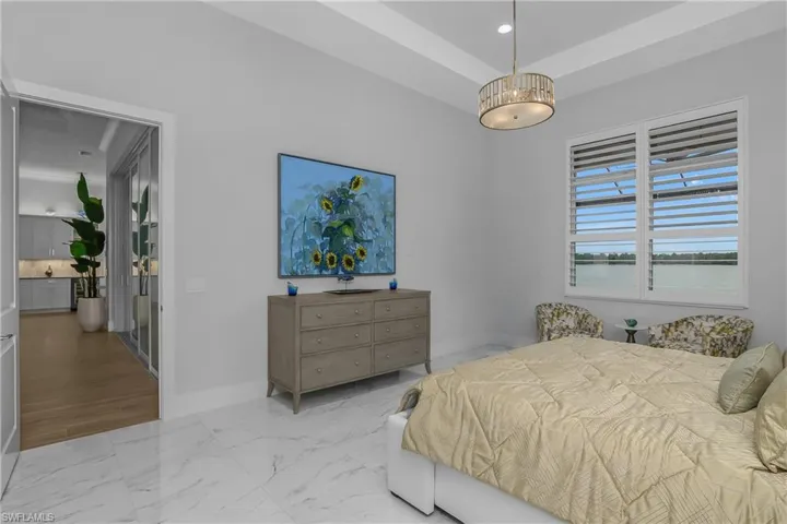 Owner suite is bright, airy and spacious and features tile flooring, custom wallpaper and plantation shutters. Photo shows room darkening drapes covering two additional windows on each side of the bed.