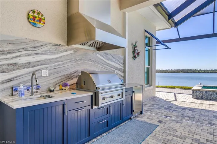 Custom outdoor kitchen includes oversized gas grill, sink, beverage cooler, overhead exhaust hood, and granite backsplash and counters.
