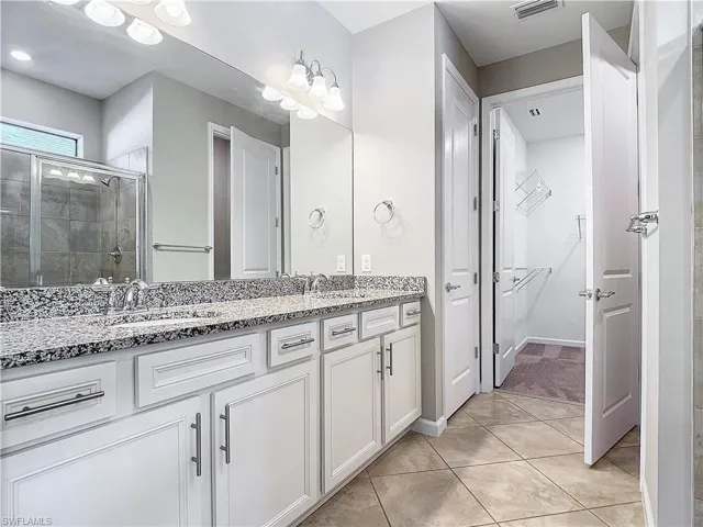 Full bath featuring double vanity, a stall shower, a walk in closet, and a sink