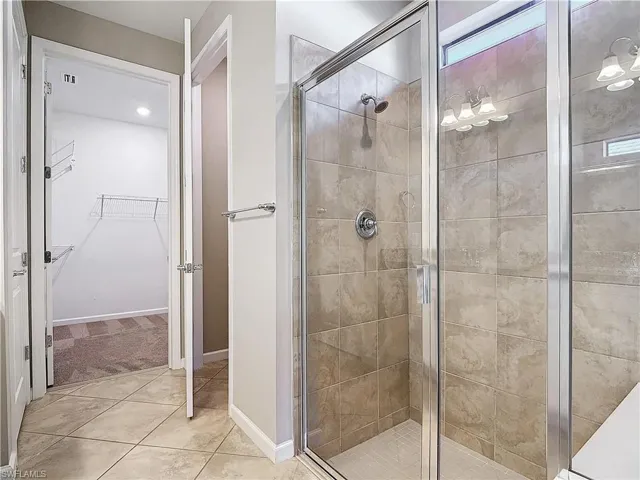 Full bath with a spacious closet, tile patterned flooring, a stall shower, and baseboards