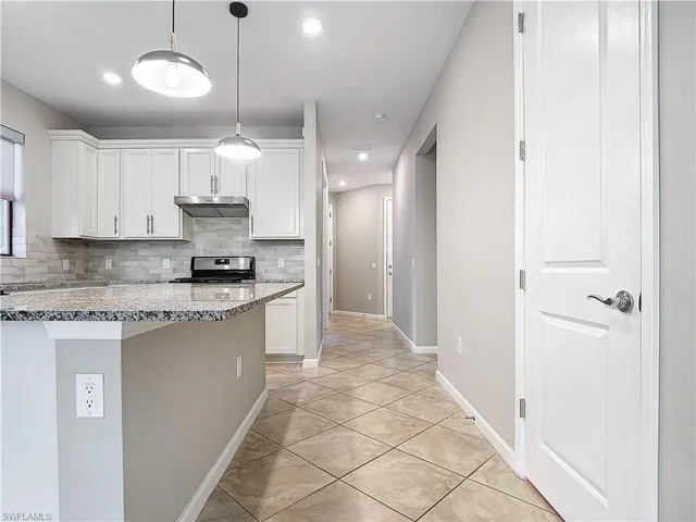 Kitchen featuring under cabinet range hood, tasteful backsplash, white cabinets, and stainless steel gas range
