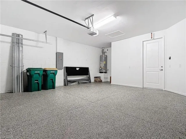 Garage with electric panel, gas water heater, a garage door opener, and concrete block wall