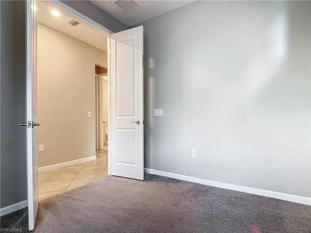 Unfurnished room with light tile patterned floors, visible vents, light colored carpet, and baseboards