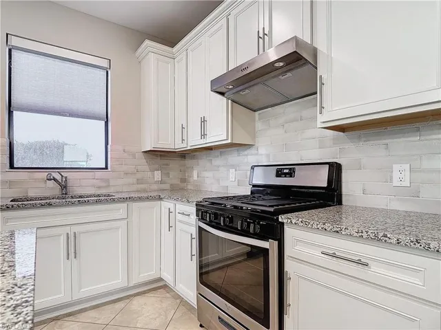 Kitchen with a sink, white cabinetry, ventilation hood, decorative backsplash, and gas range