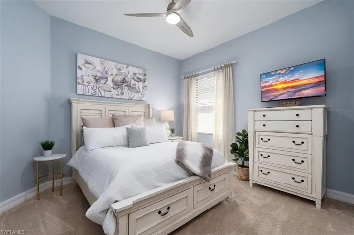 Spacious room featuring neutral carpeting, light blue wall paint, a ceiling fan with integrated lighting, and a window with blinds and drapes
