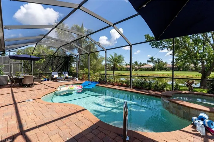 Screened outdoor living area featuring a freeform pool, integrated spa, and brick paver patio