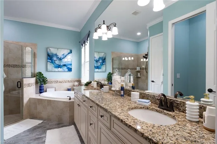 Double vanity with a granite countertop and dual oval sinks, a built-in jetted tub, a tiled walk-in shower with a glass enclosure, and wood-finish cabinetry