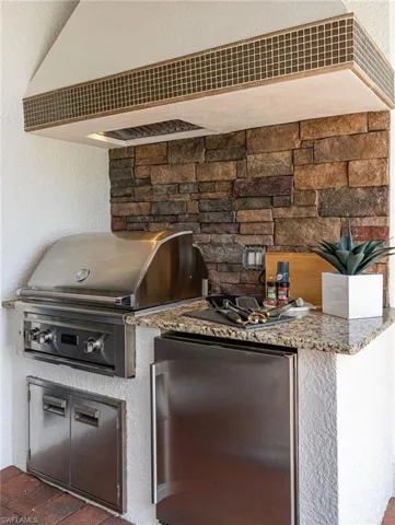 Outdoor kitchen featuring stacked stone backsplash, stainless steel grill, under-counter refrigerator, built-in storage, and granite countertop