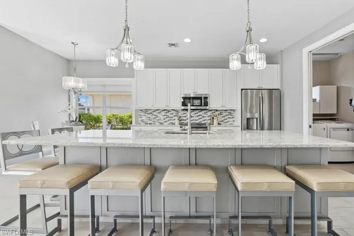 Kitchen featuring tasteful backsplash, visible vents, appliances with stainless steel finishes, a notable chandelier, and washer and clothes dryer