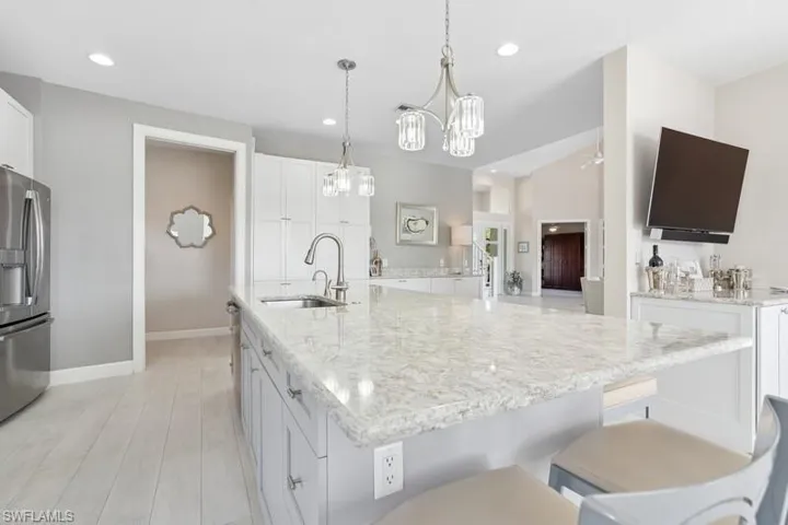 Kitchen featuring stainless steel fridge with ice dispenser, white cabinetry, light stone counters, a sink, and a spacious island