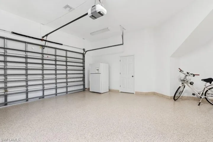 Garage featuring a garage door opener, visible vents, white fridge with ice dispenser, and baseboards