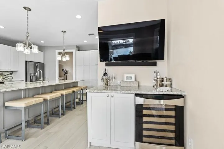 Bar with light wood-style flooring, visible vents, stainless steel fridge, pendant lighting, and beverage cooler