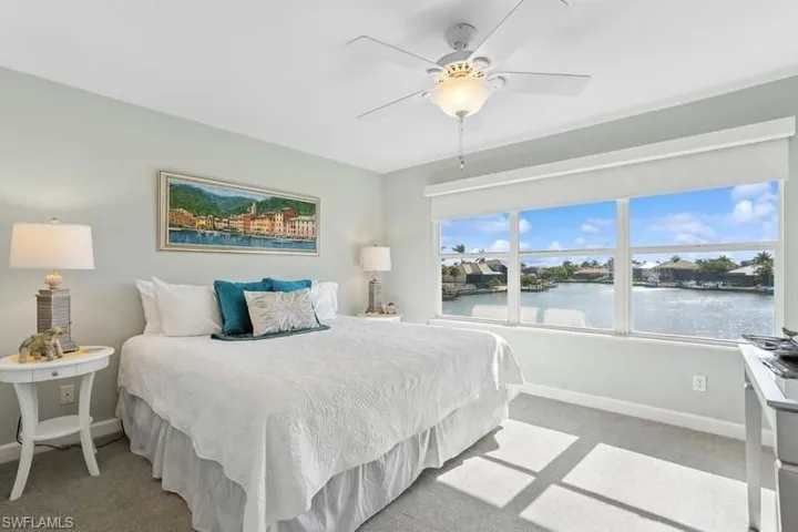 Bedroom featuring a water view, baseboards, a ceiling fan, and light colored carpet