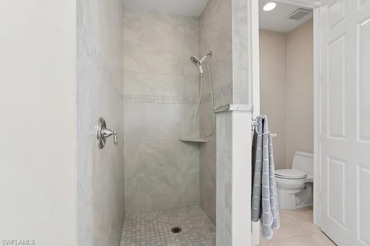 Full bathroom with a tile shower, tile patterned floors, visible vents, and toilet