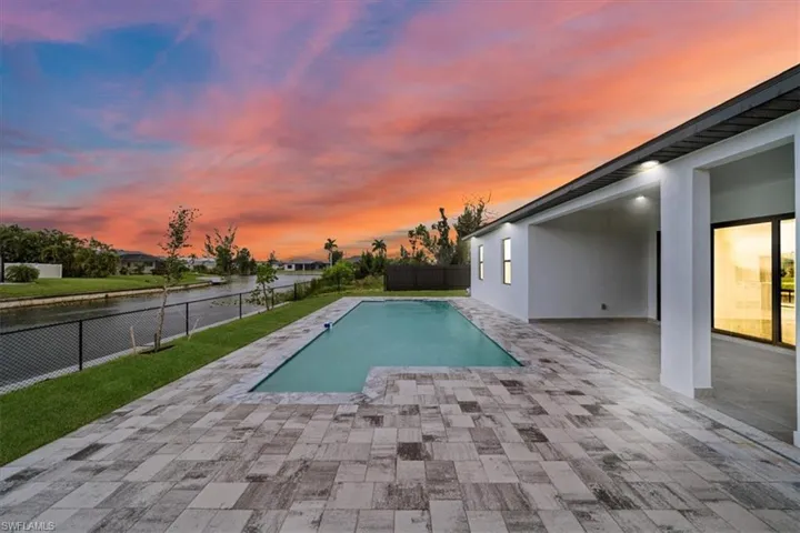 Pool at dusk with a fenced backyard, a patio area, and a water view