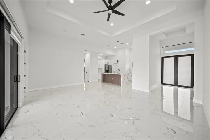 Unfurnished living room with a raised ceiling, recessed lighting, french doors, and light marble finish flooring