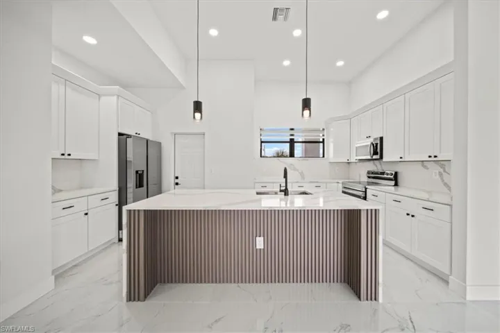 Kitchen with light stone countertops, stainless steel appliances, light marble finish flooring, recessed lighting, and white cabinetry