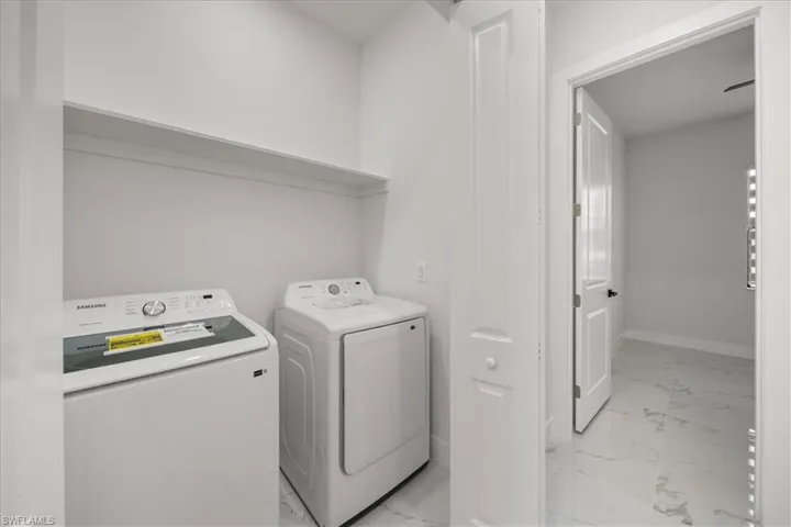 Laundry area with light marble finish floors and washer and clothes dryer