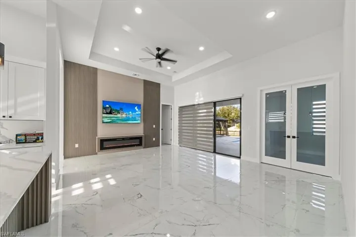 Unfurnished room with french doors, light marble finish floors, a glass covered fireplace, and recessed lighting