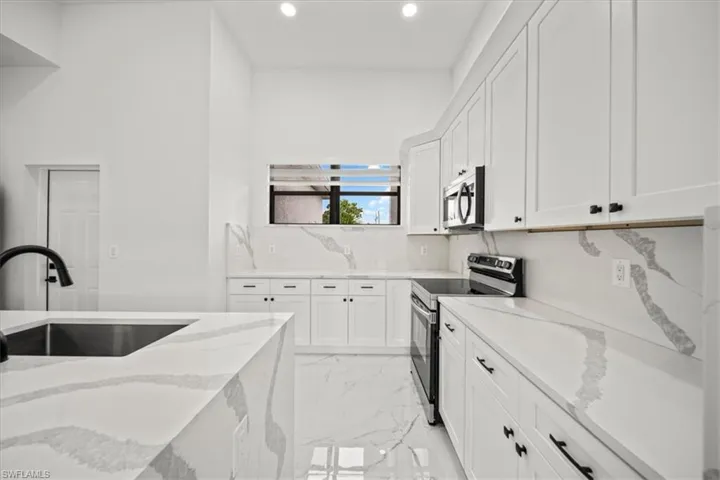 Kitchen with appliances with stainless steel finishes, light stone countertops, white cabinets, light marble finish flooring, and recessed lighting