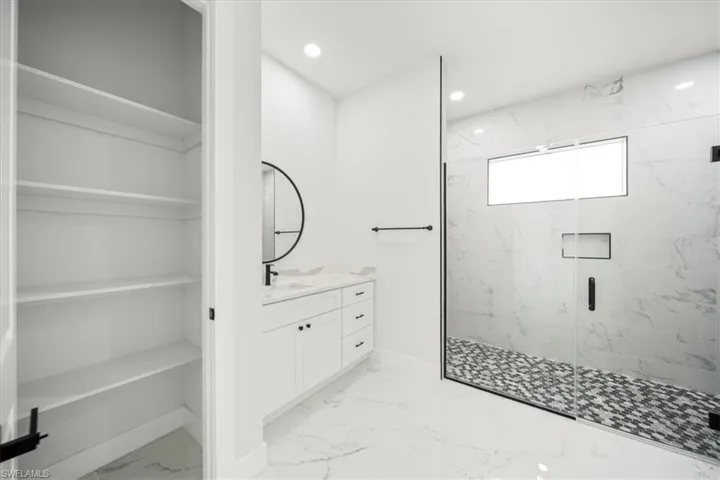 Full bath featuring vanity, a marble finish shower, light marble finish flooring, recessed lighting, and a walk in closet