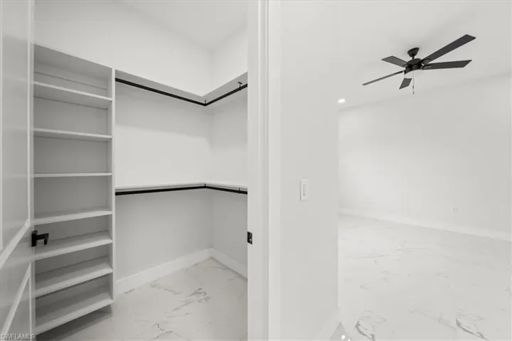 Spacious closet featuring light marble finish flooring and a ceiling fan