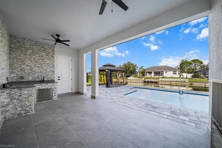 View of pool with an outdoor kitchen, ceiling fan, a patio, a gazebo, and a water view