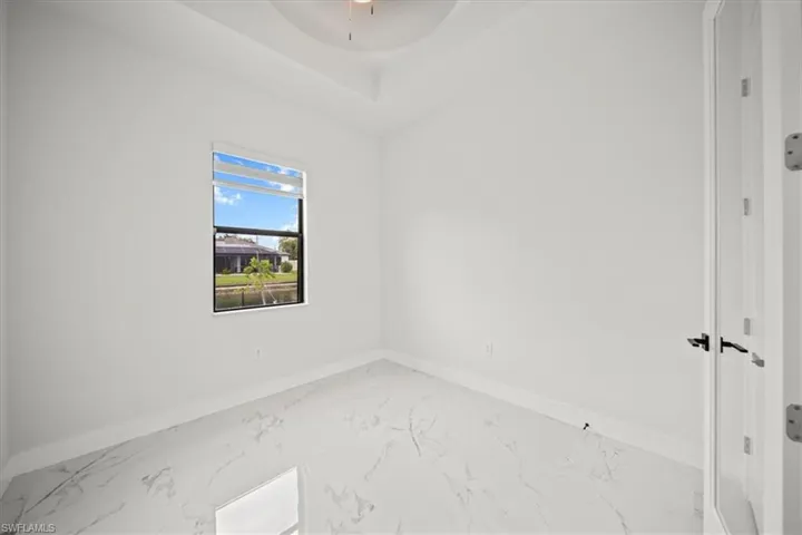 Empty room with marble look tile flooring, a raised ceiling, and ceiling fan