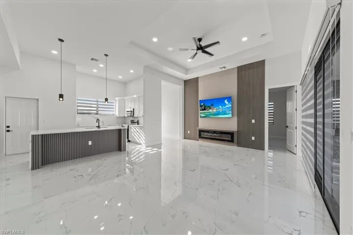 Living room with a raised ceiling, ceiling fan, recessed lighting, light marble finish floors, and a towering ceiling