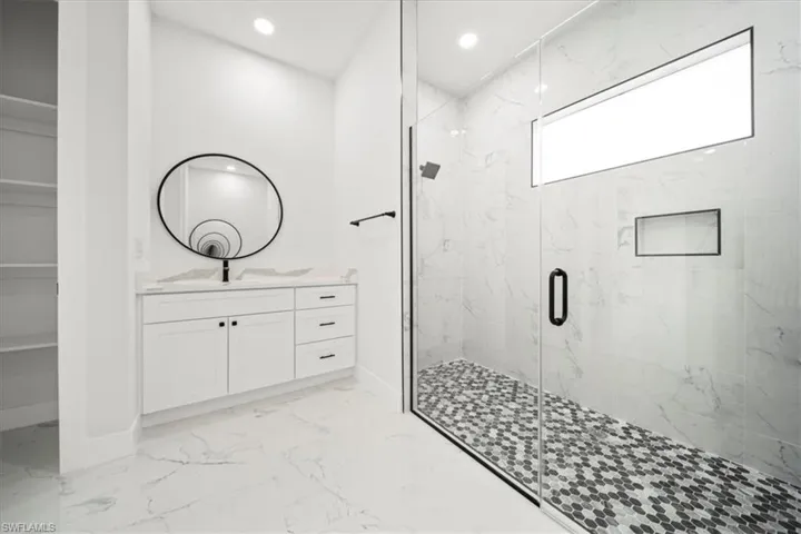 Bathroom with a marble finish shower, vanity, light marble finish floors, and recessed lighting