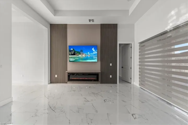 Unfurnished living room with a glass covered fireplace, light marble finish floors, and a raised ceiling