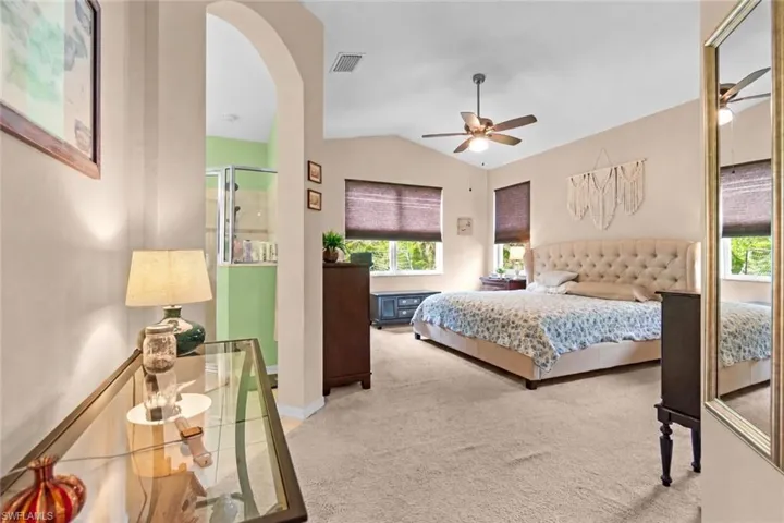 Primary bedroom with vaulted ceiling and light colored carpet