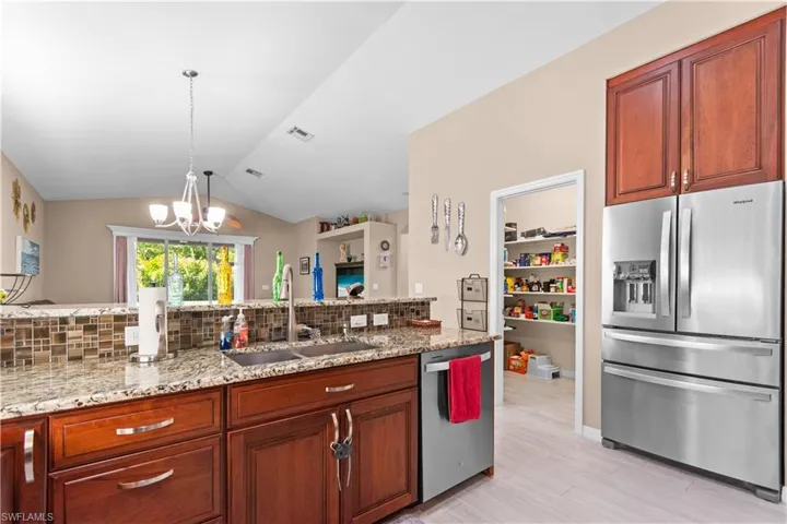 Kitchen featuring stainless steel appliances, granite counters, vaulted ceiling, and walk-in pantry