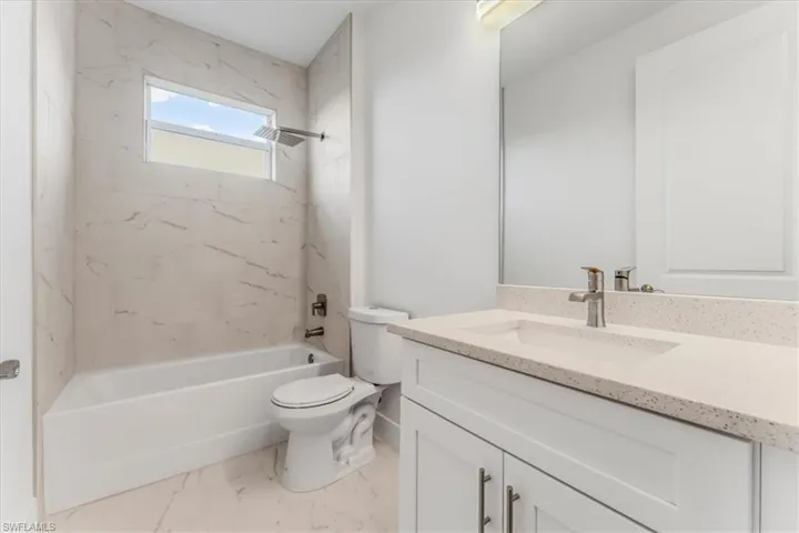 Full bath featuring vanity,  shower combination, and marble look tile flooring