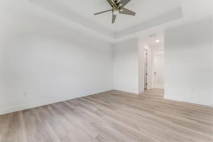 Empty room with a tray ceiling, light wood finished floors, a ceiling fan, and recessed lighting