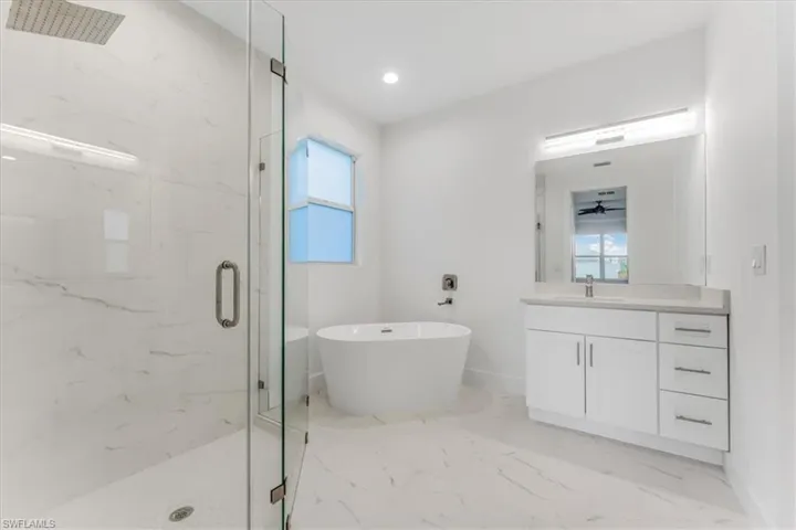 Full bathroom featuring a marble finish shower, a freestanding tub, vanity, marble finish floors, and recessed lighting