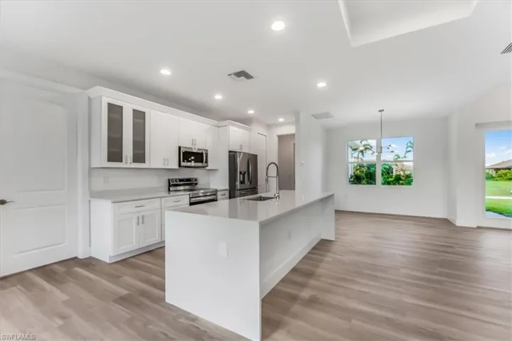 Kitchen with stainless steel appliances, a center island with sink, light wood-style flooring, white cabinetry, and light countertops