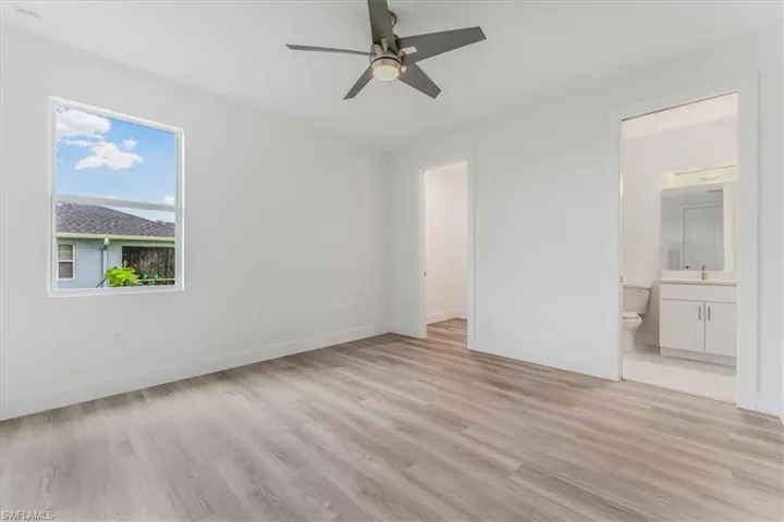 Unfurnished bedroom featuring light wood-style floors, ensuite bathroom, and a ceiling fan