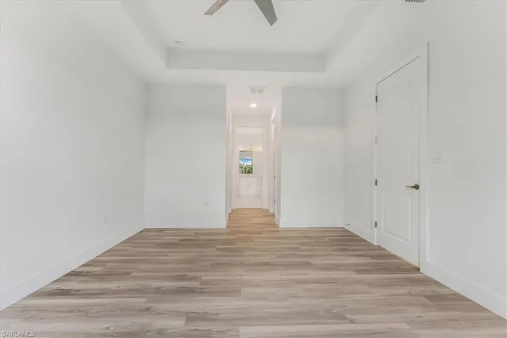 Spare room with a tray ceiling, a ceiling fan, and light wood-style flooring
