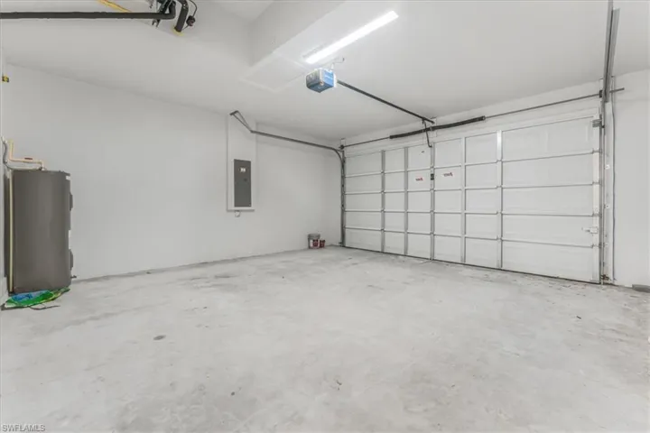 Garage with water heater, electric panel, and a garage door opener